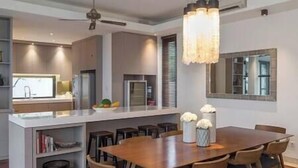 A modern kitchen with a central island, a dining area with a wooden table and chairs, and a chandelier.