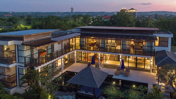 A modern multi-story house with large windows, a balcony, and a view of the surrounding landscape.