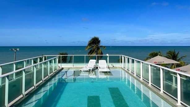 A clear blue sky, a swimming pool with lounge chairs, and a view of the ocean. - CABO BRANCO BEACHFRONT FLAT at the Green Sunset Hotel (João Pessoa)