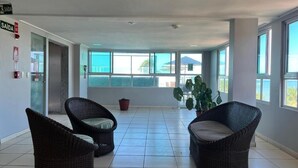 A spacious room with two wicker chairs, a potted plant, and a view of the ocean through large windows. - CABO BRANCO BEACHFRONT FLAT at the Green Sunset Hotel (João Pessoa)