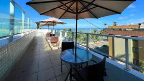 A balcony with glass railings, a glass table, and two umbrellas. - CABO BRANCO BEACHFRONT FLAT at the Green Sunset Hotel (João Pessoa)