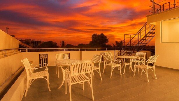 Terraza en la azotea con sillas y una mesa blancas, con vistas a un atardecer de colores intensos.