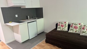 A compact kitchen with white cabinets, a dishwasher, and a grey backsplash. A brown sofa with floral cushions is positioned against the wall. - Big Studio Apartment in Sollentuna, Stockholm (Sollentuna)
