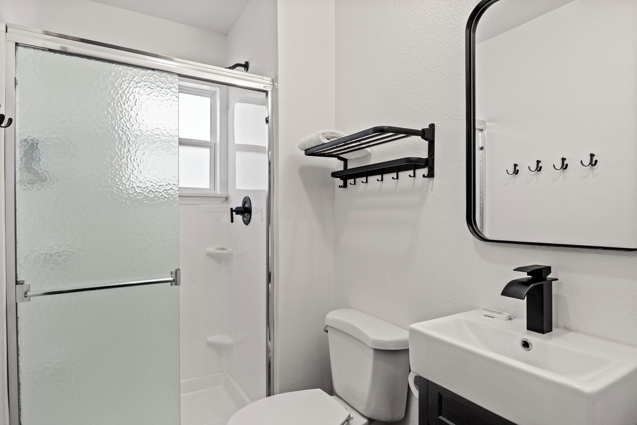 A bathroom with a white toilet, a white sink with a black faucet, a towel rack, and a glass shower door.