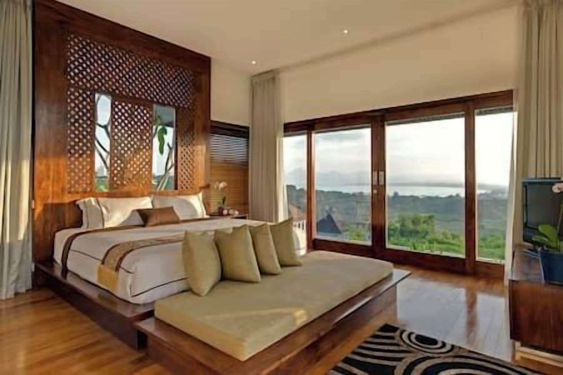 A bedroom with a large bed, a view of the outdoors, and a wooden headboard.