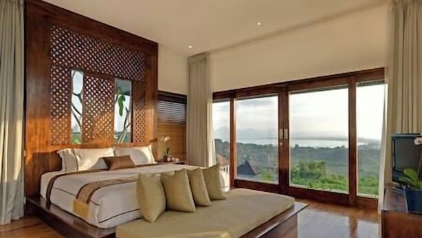 Ein Schlafzimmer mit einem großen Bett, Blick ins Freie und einem hölzernen Kopfteil.