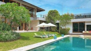 Ein modernes Haus mit Schwimmbad, Sitzgelegenheiten im Freien und üppigem Grün.