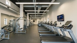 Une salle de sport équipée de tapis de course, d’appareils de musculation et d’un écran de télévision diffusant une chaîne d’information.