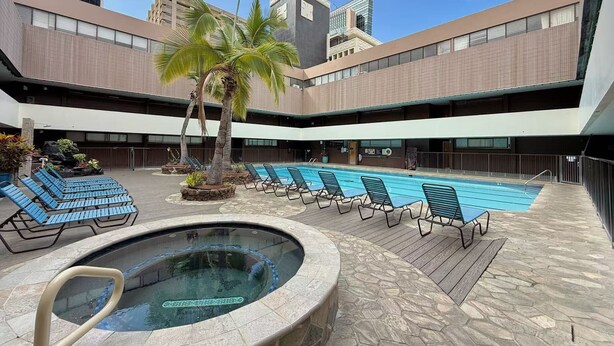 Un espace piscine doté de chaises longues et d’un jacuzzi, entouré d’un bâtiment moderne à plusieurs étages et doté de grandes fenêtres.