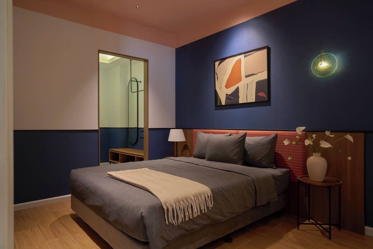 A modern bedroom with a large bed, a bedside table, a mirror, and a wall-mounted abstract painting.