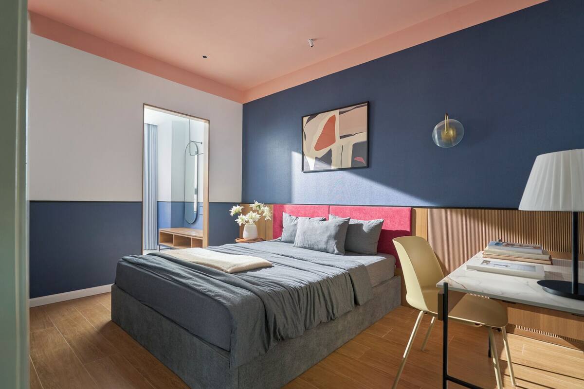 A modern bedroom with a bed, bedside table, chair, and a desk with a lamp.
