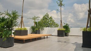 Una terraza en la azotea con un banco de madera, plantas en macetas y vistas del horizonte de la ciudad.