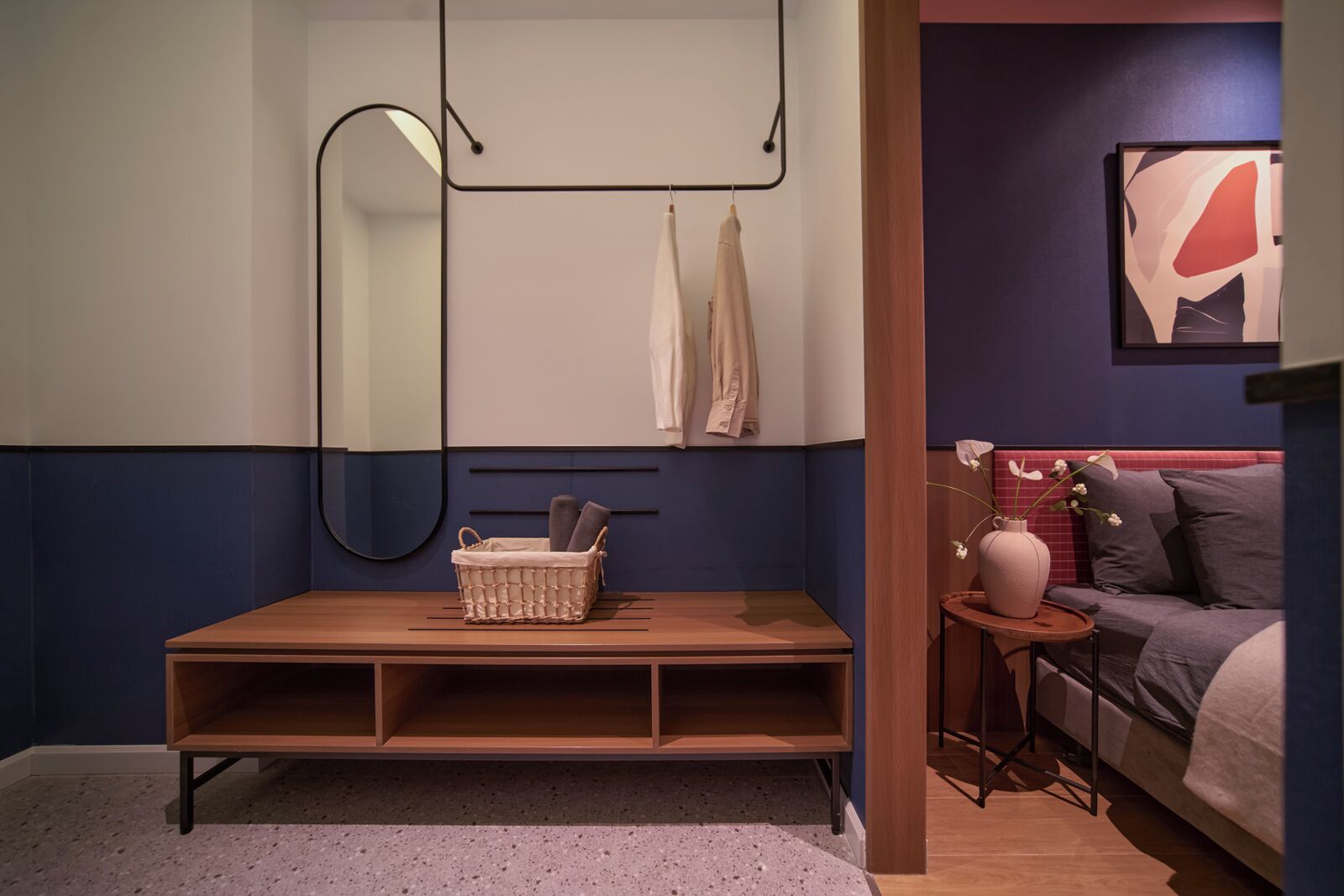 Um quarto com cama, mesa de cabeceira, uma pequena mesa com um vaso e espelho fixado na parede.