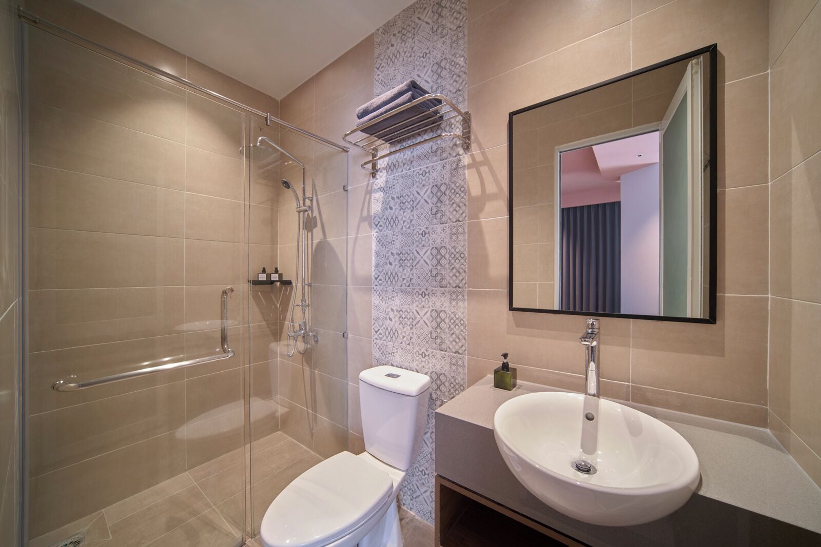 A modern bathroom with a glass shower enclosure, a white toilet, a sink with a mirror, and patterned tiles on the walls.