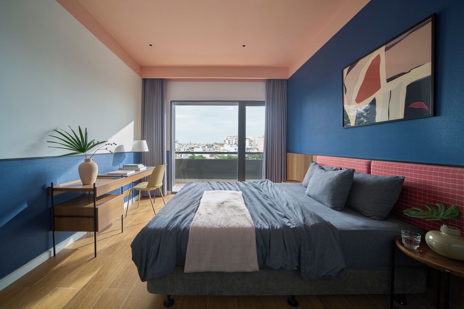 A modern bedroom with a large bed, a desk, a chair, and a view of the city through a large window.