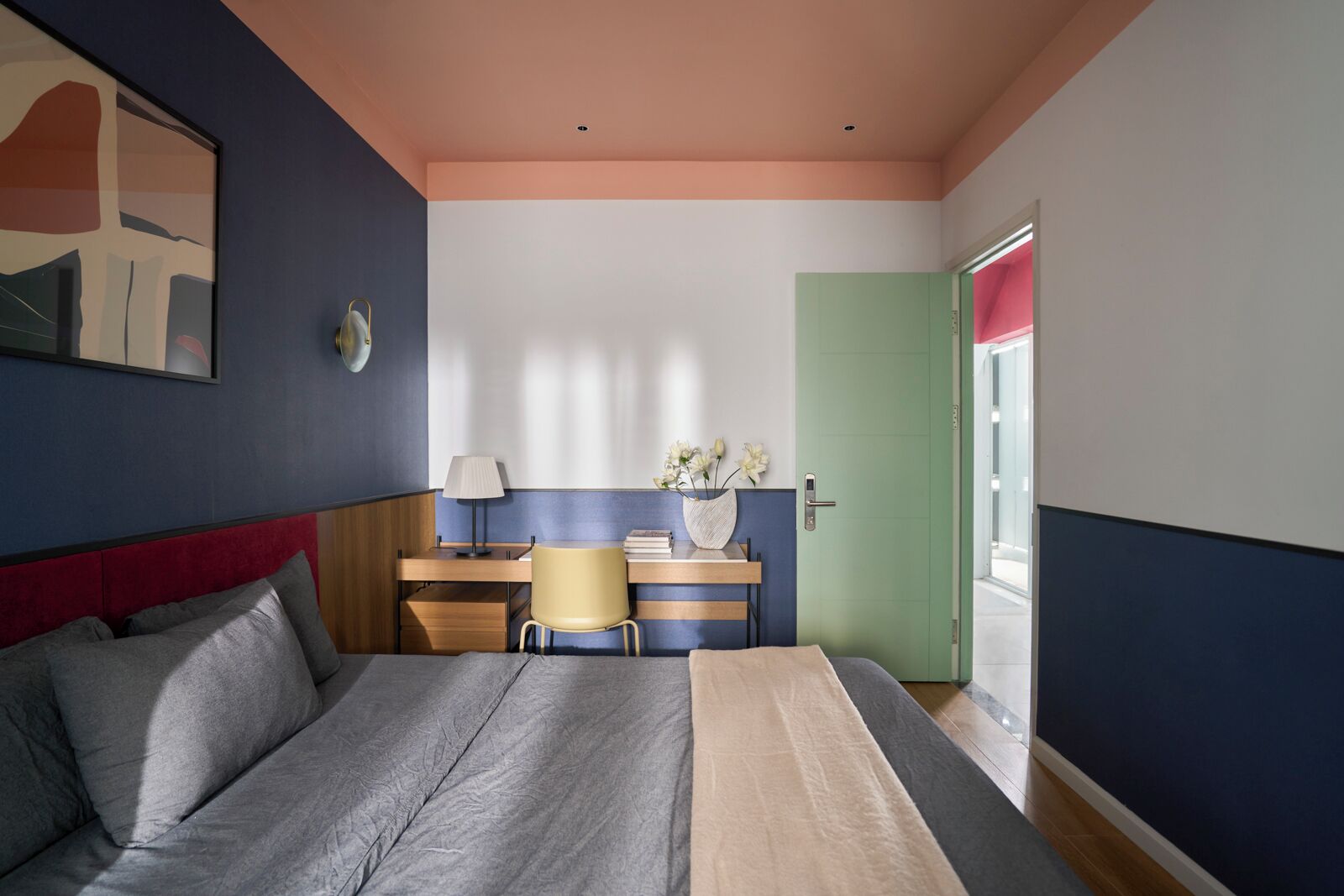A bedroom with a bed, a desk, a chair, a lamp, and a door.