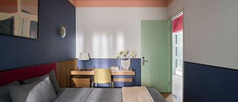 A bedroom with a bed, a desk, a chair, a lamp, and a door.