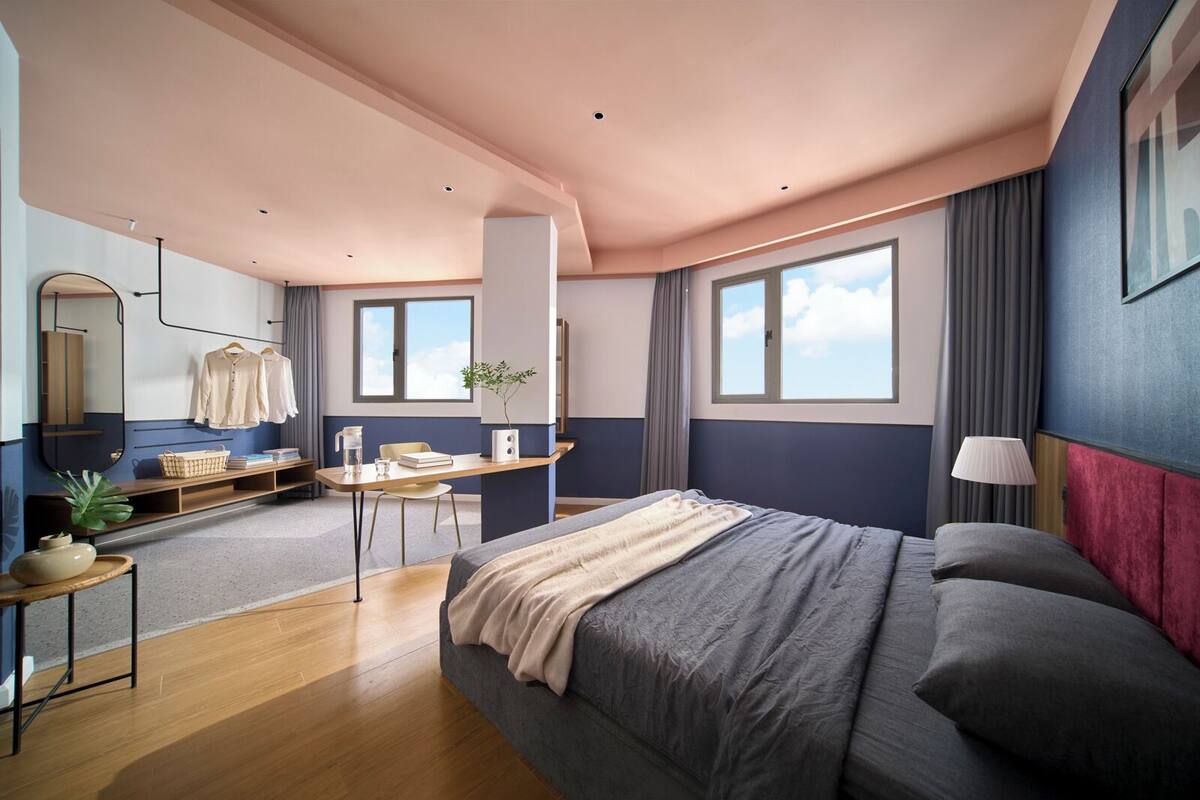 A modern bedroom with a large bed, a desk, a chair, a mirror, and a window.