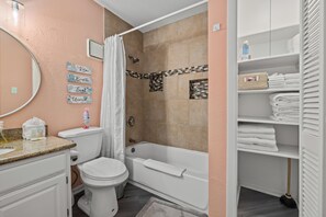 A bathroom with a toilet, sink, shower, and bathtub. There are towels and toiletries on the shelves.
