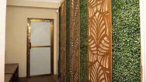 A hallway with a decorative wooden panel, a door with a frosted glass panel, and a wall covered with green foliage. - Aarya Wellness & Hostel  (Kathmandu)