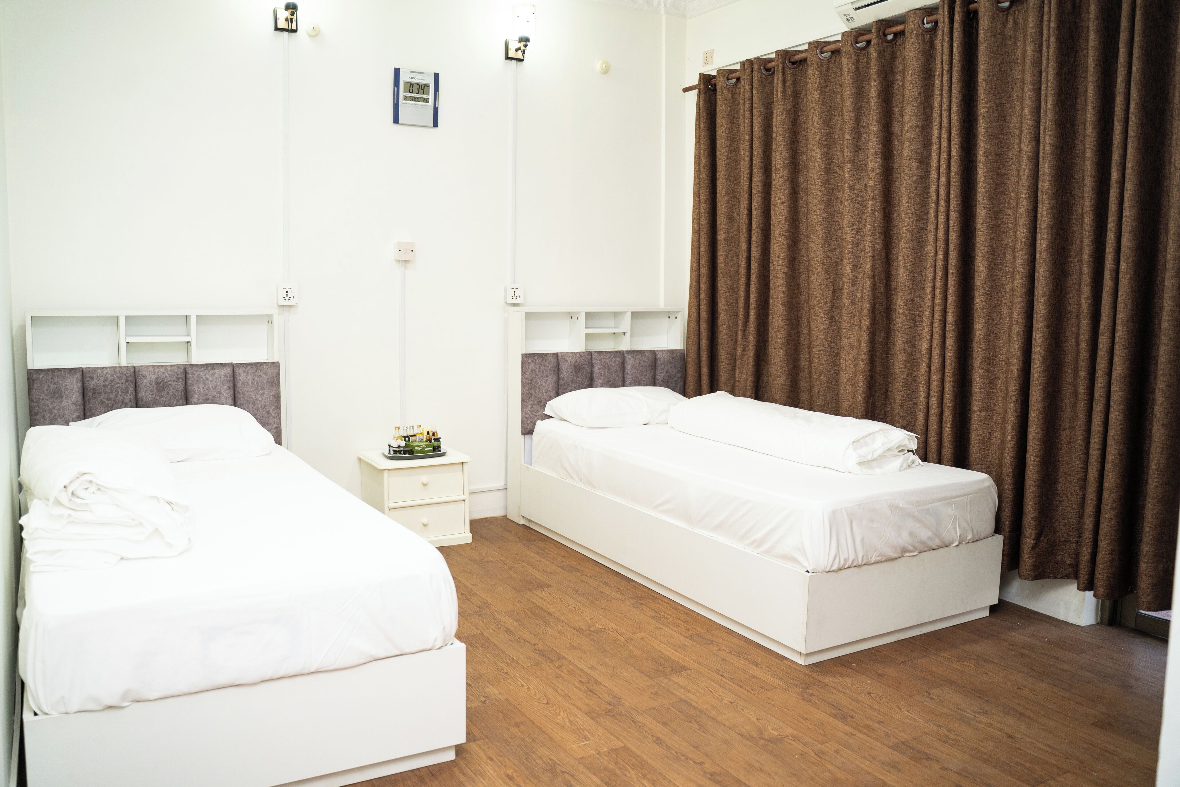 A hotel room with two single beds, a nightstand, and a large window with curtains.