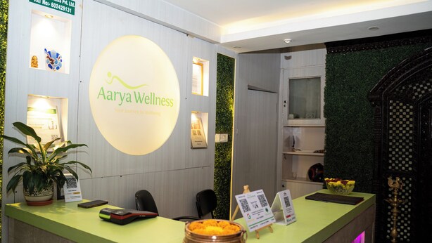 A reception desk with a green counter, a logo for Aarya Wellness, a potted plant, a smartphone, a cash register, and a decorative bowl. - Aarya Wellness & Hostel  (Kathmandu)