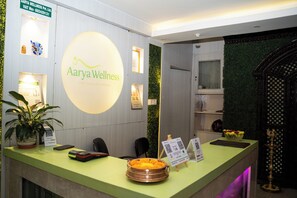 A reception desk with a green counter, a logo for Aarya Wellness, a potted plant, a smartphone, a cash register, and a decorative bowl. - Aarya Wellness & Hostel  (Kathmandu)