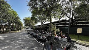 Calle flanqueada por coches deportivos estacionados y un cartel que indica zona de valet.