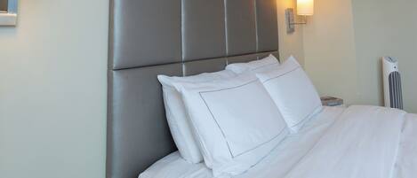 A hotel room with a bed, a bedside table with a clock, and a wall-mounted artwork.