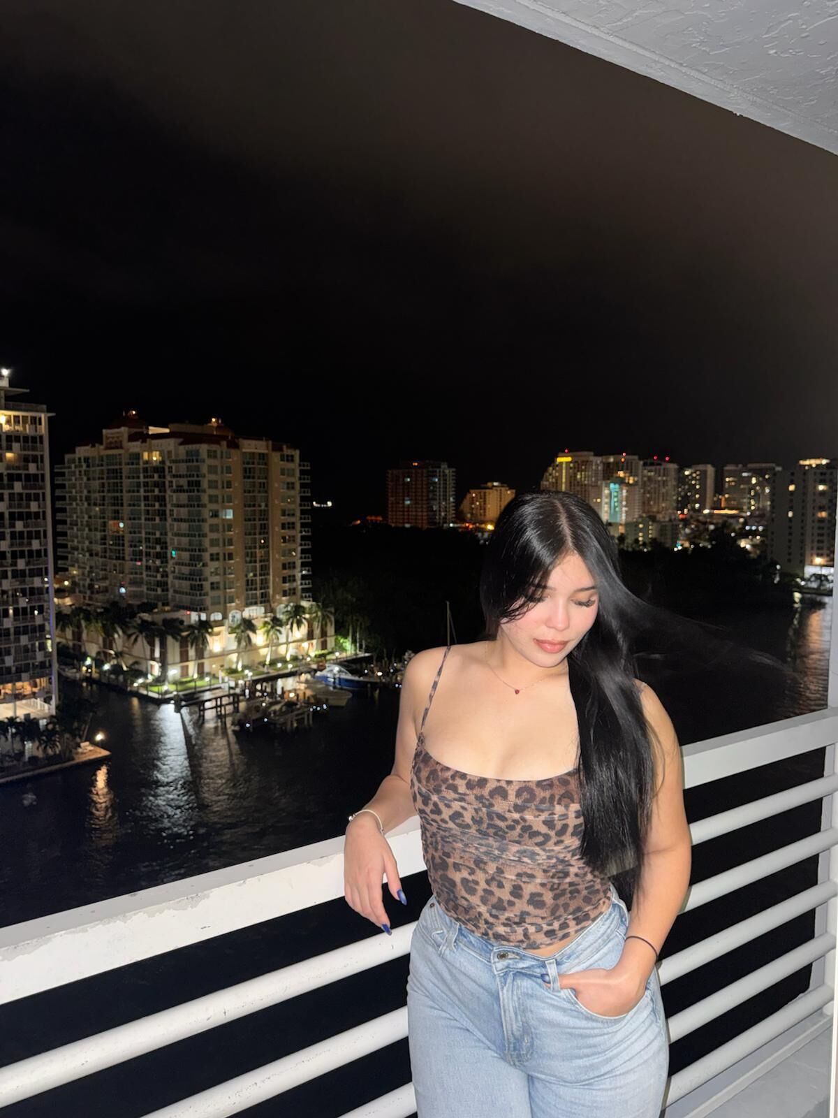 Un balcon offrant une vue sur la ville la nuit, avec des bâtiments et un port de plaisance.