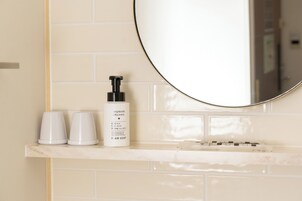 A bathroom vanity with a white marble countertop, a round mirror, and two white cups.