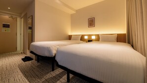 Ein Hotelzimmer mit zwei Betten, einem Holz-Kopfteil, einer Wandleuchte und einer Tür.