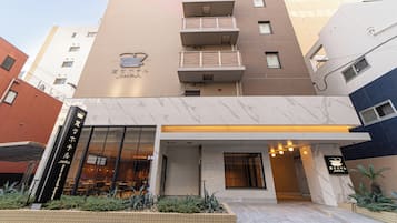 A hotel entrance with a tiled facade, a visible signboard, and a small garden area with plants.