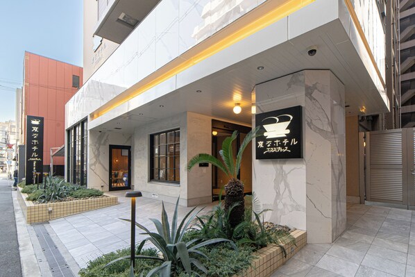 A modern building with a large entrance, a signboard, and a well-maintained garden area.