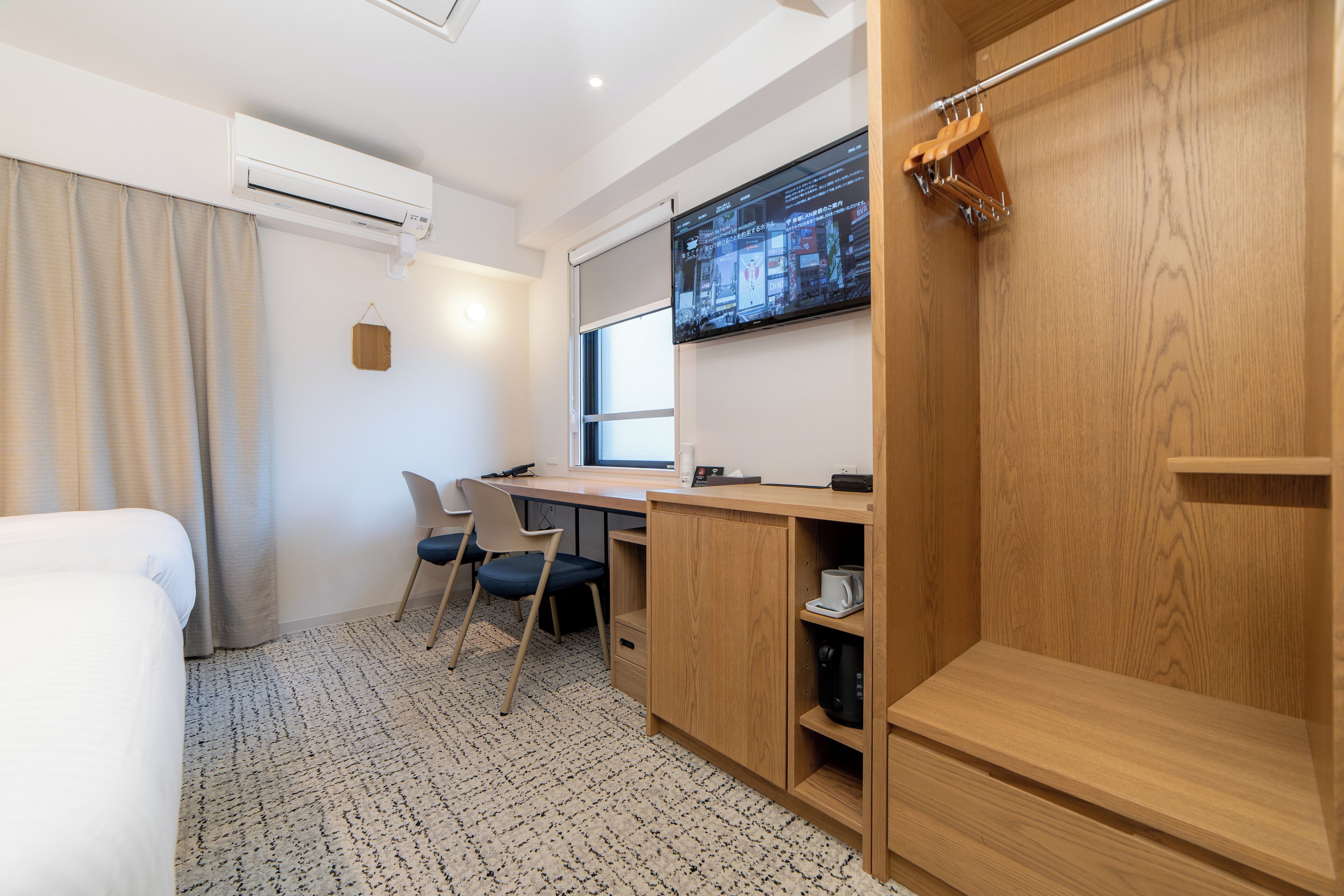 A hotel room with a bed, desk, chairs, and a TV.