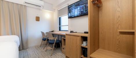 A hotel room with a bed, desk, chairs, and a TV.