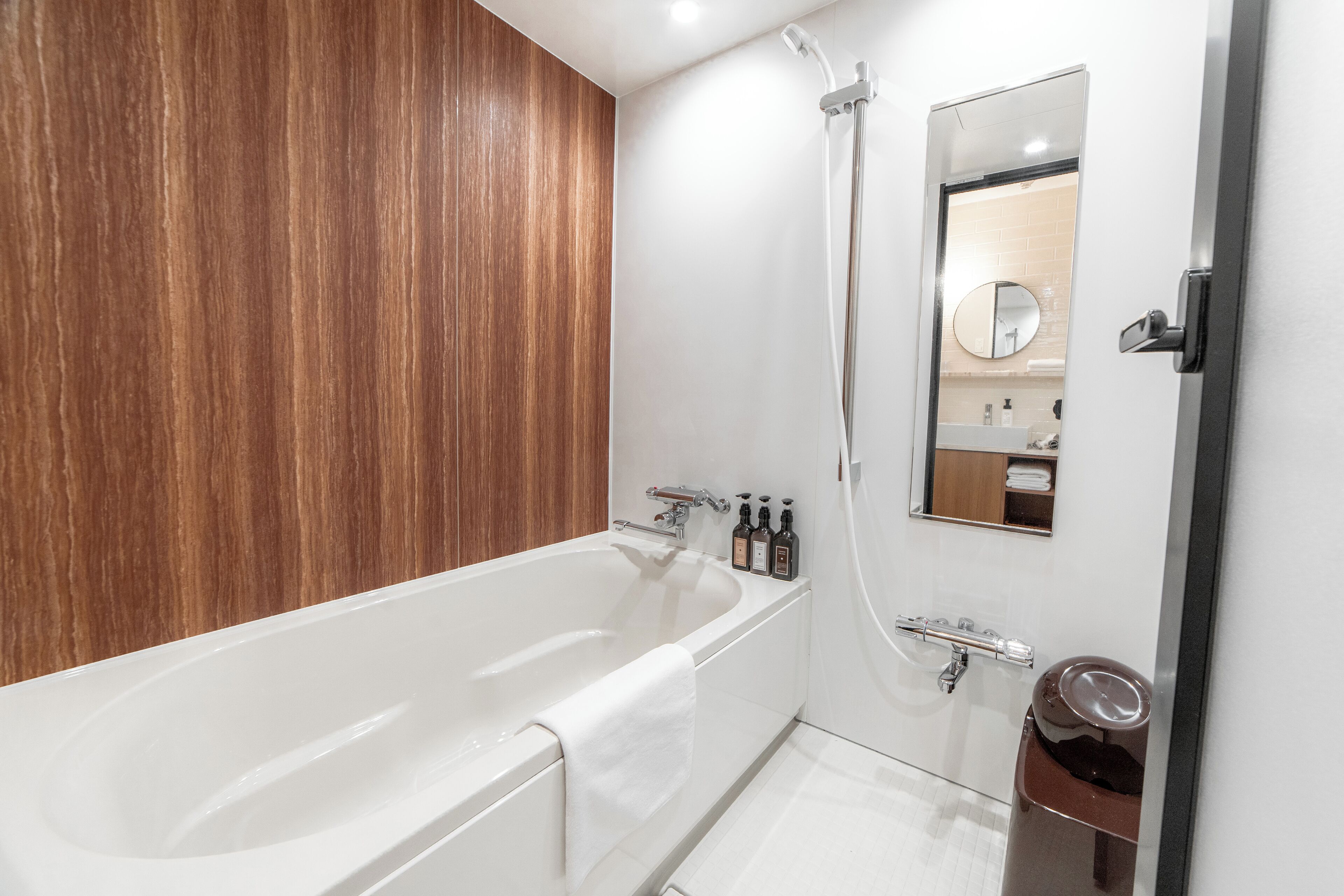 Ein modernes Badezimmer mit einer Holzpaneelwand, einer weißen Badewanne, einer Duschkabine, einem Spiegel und einem Mülleimer.