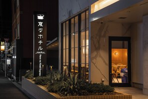 L’entrée d’un hôtel, avec une enseigne indiquant « Hema no Hotel Express », et un intérieur bien éclairé visible à travers les portes vitrées.