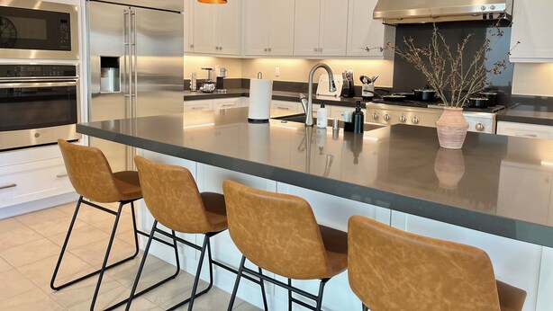 Una cocina moderna con armarios blancos, electrodomésticos de acero inoxidable, una isla central con taburetes y luminarias colgantes.