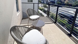 Un balcón con sillas de mimbre y una pequeña mesa, con vistas a una zona residencial con casas modernas.
