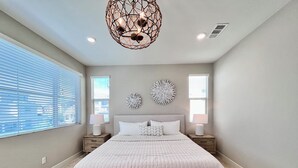 Un dormitorio con una cama grande, dos mesitas de noche, un banco de madera, una lámpara decorativa en el techo y una obra de arte en la pared.