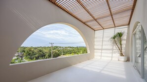 Un balcón moderno con un muro blanco curvo, techo de madera y una planta en maceta.