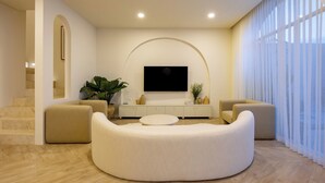 Una sala de estar moderna con un sofá curvo, un televisor de pantalla plana, una consola blanca y una escalera que sube a otro nivel.