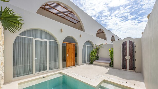 Un área de piscina moderna con una piscina cristalina, ventanas arqueadas y una puerta de madera.