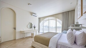 Un dormitorio moderno con una cama grande, una mesita de noche, un espejo y vistas al exterior a través de amplias ventanas.