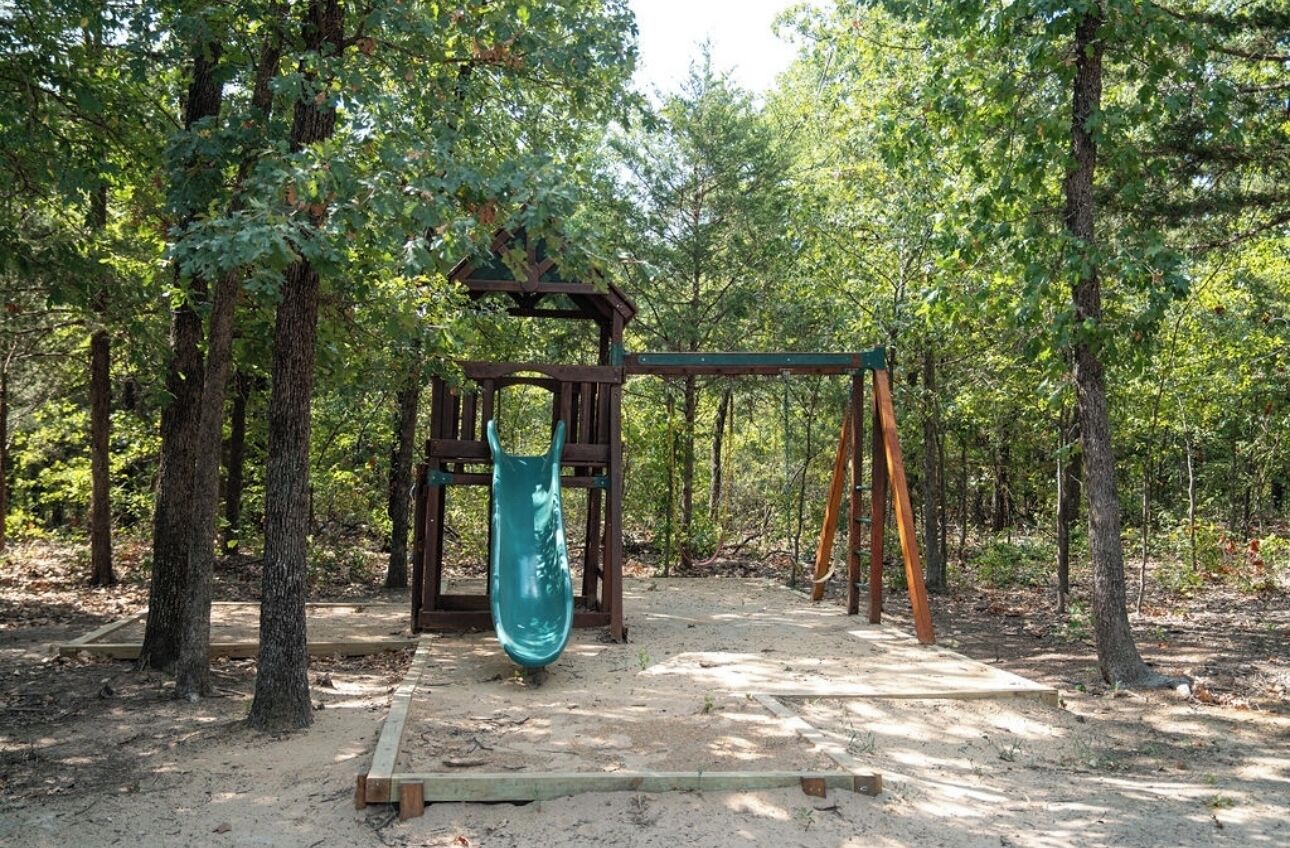 A playground with a swing set and a slide in a wooded area.