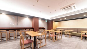 Interior de un restaurante con mesas y sillas de madera, una zona de estar con un banco acolchado y un equipo de aire acondicionado instalado en la pared.