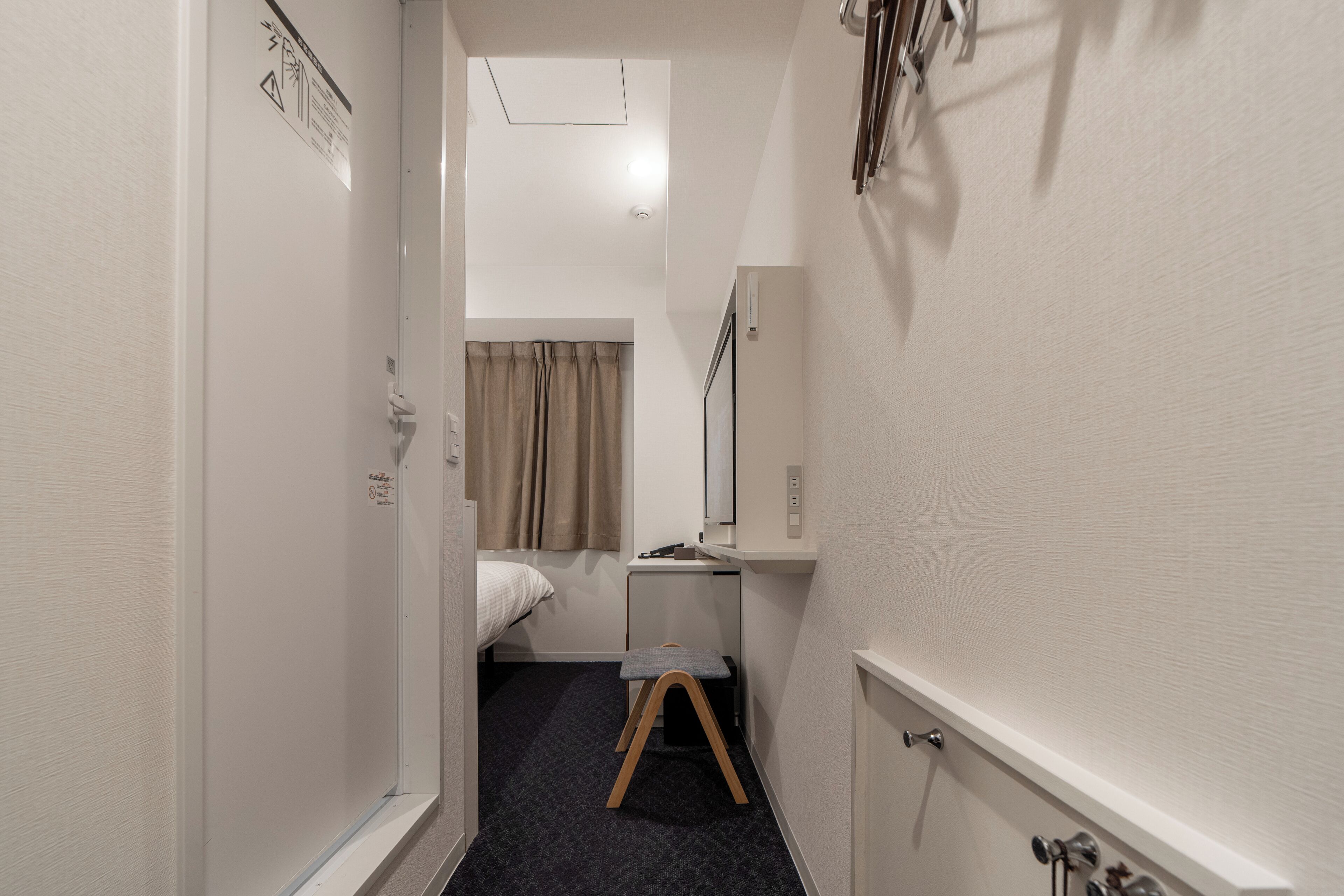 A narrow hallway with a bed, a small desk, a mirror, and a step stool.