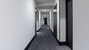 Un pasillo largo y estrecho con piso alfombrado y puertas a ambos lados que dan a habitaciones.