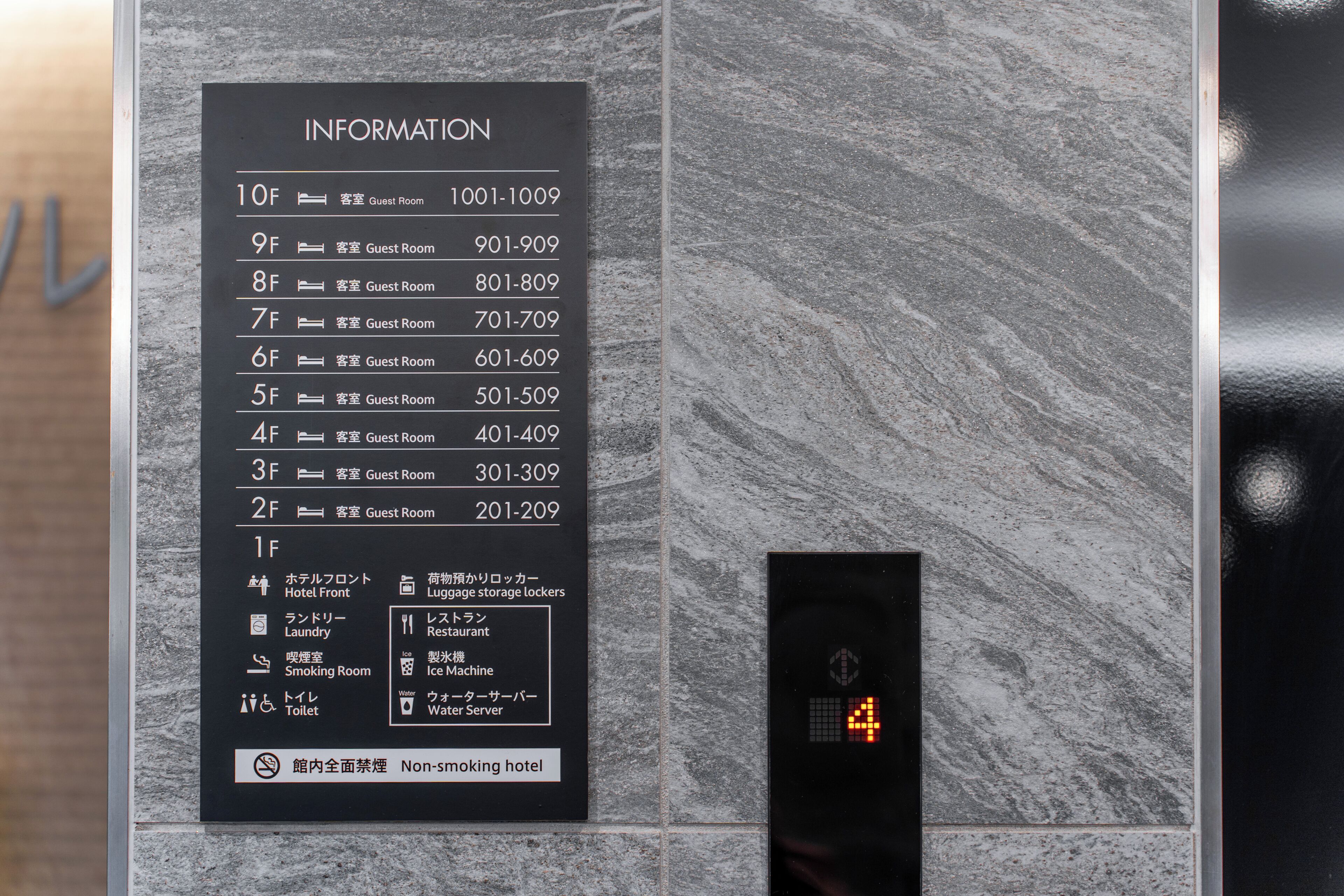 A hotel information board with room numbers and guest room details, a digital elevator display, and a non-smoking hotel notice.